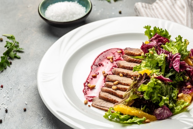 Salada com pato assado, mistura para salada verde e molho de frutas vermelhas.