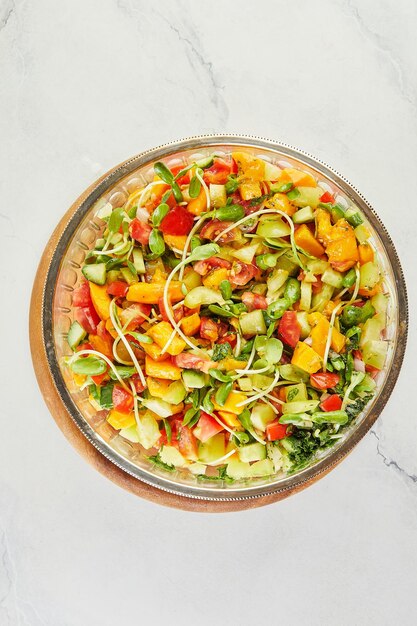 Salada com pepino, tomate, manga e microgreens em saladeira de vidro em suporte de madeira