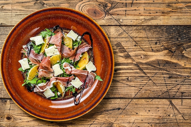 Salada com presunto de parma, queijo parmesão, rúcula e tangerina no prato.