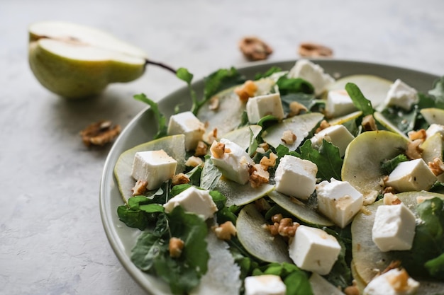 Salada com queijo feta de pêra rúcula e nozes Salada de delicadeza em um prato sobre fundo cinza