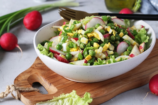 Salada com rabanete, cebolinha, ovos e ervilhas, temperada com azeite em prato sobre tábua de madeira. fechar-se