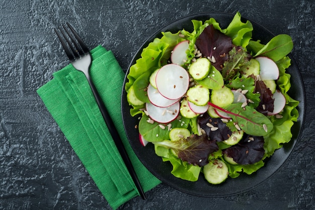 Salada com rabanetes frescos, rúcula, beterraba, acelga, sementes de girassol, sementes de linho e gergelim em um fundo preto