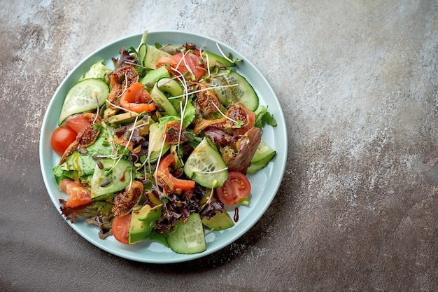 Salada com salmão, abacate, tomate e alcachofra em um prato azul sobre fundo marrom