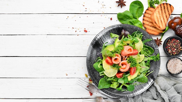 Salada com salmão abacate, tomate e espinafre Em um prato preto sobre um fundo de madeira Vista superior Espaço livre para o seu texto Postura plana