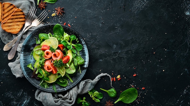 Salada com salmão, abacate, tomate e espinafre. Em uma placa preta em uma vista superior de fundo de madeira. Espaço livre para o seu texto. Postura plana