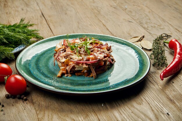 Salada com tomate, conservas de cogumelos, cebola e carne cozida num prato azul sobre uma superfície de madeira. Salada eslava medina. Fechar-se