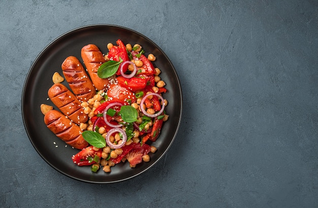 Salada com tomate de grão de bico e sementes de gergelim e salsichas em um fundo escuro