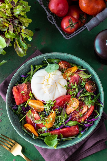 Salada com tomate, rúcula, queijo Burrata e microgreens em um fundo de pedra verde, vista de cima, vertical