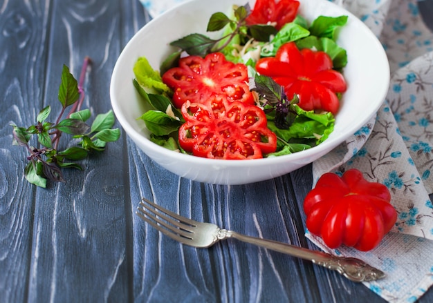 Foto salada com tomate vermelho maduro grande com manjericão em uma mesa de madeira