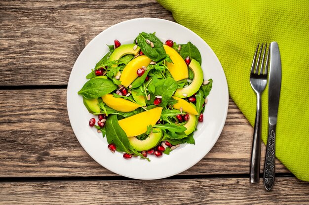 Salada de abacate com espinafre e romã em um prato branco sobre uma mesa de madeira