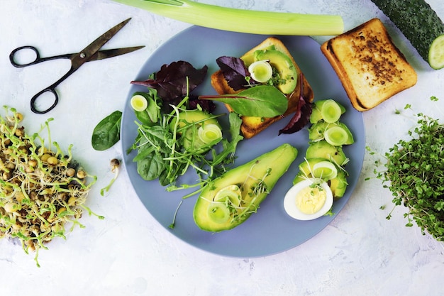 Salada de abacate, ovos cozidos, alho-poró, brotos de micro-verduras e rúcula, em um prato sobre uma mesa de luz