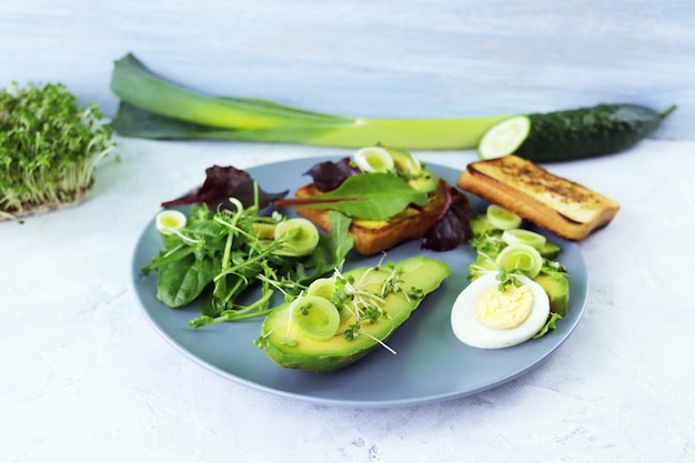 Salada de abacate ovos cozidos alho-poró micro verdes brotos e rúcula em um prato sobre uma mesa de luz