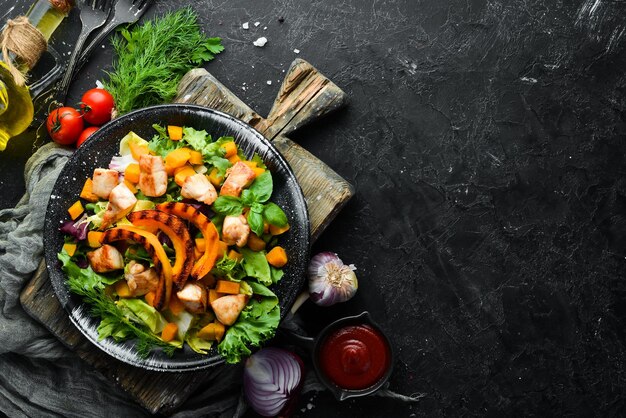 Salada de abóbora com carne de frango e legumes em um prato preto sobre um fundo preto Vista superior Espaço livre para o seu texto