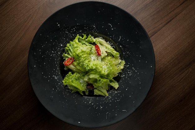 Salada de alface pimentão queijo parmesão em um prato preto Salada em um prato preto