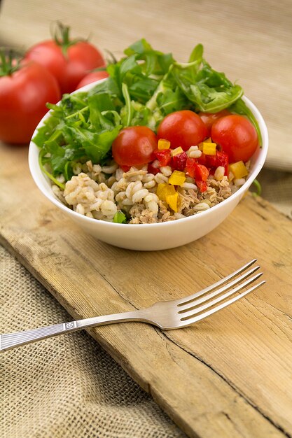 Salada de atum em tigela branca e garfo, superfície de madeira