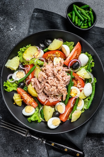 Salada de atum nicoise com legumes, ovos e anchovas em um prato. Fundo preto. vista do topo.