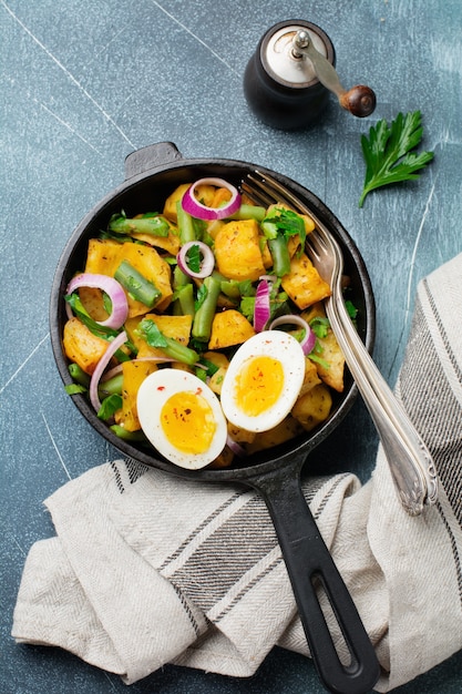 Salada de batata quente com feijão verde, pimenta, salsa, ovos e cebola roxa na frigideira na mesa de concreto cinza. Foco seletivo. Vista do topo. Copie o espaço.