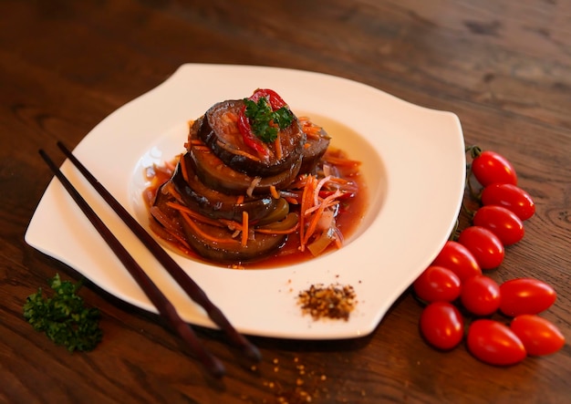 Salada de berinjela com cenoura ao estilo coreano com tomate em uma mesa de madeira escura