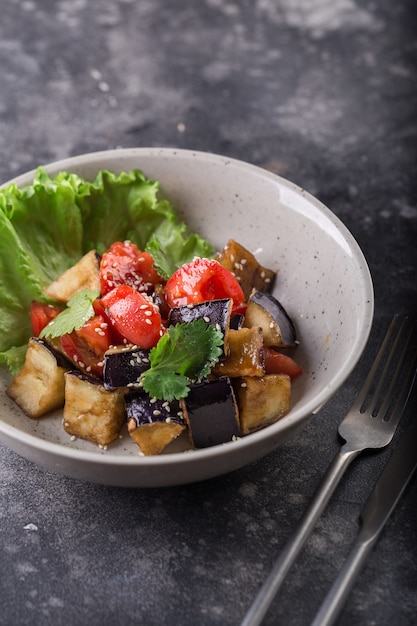 Salada de berinjela e tomate cozida com sementes de alface e gergelim em um prato branco.