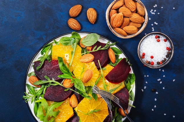 Salada de beterraba fresca com rúcula laranja e amêndoas em fundo azul Comida de verão saudável vegana Configuração plana Espaço de cópia