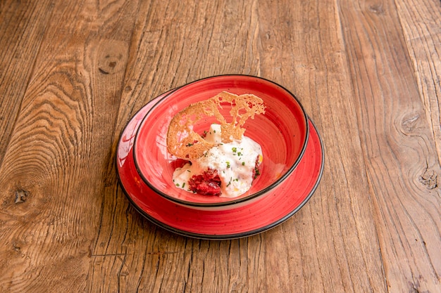 Salada de burrata italiana com crocante por cima sobre tigela vermelha e prato vermelho na mesa de madeira