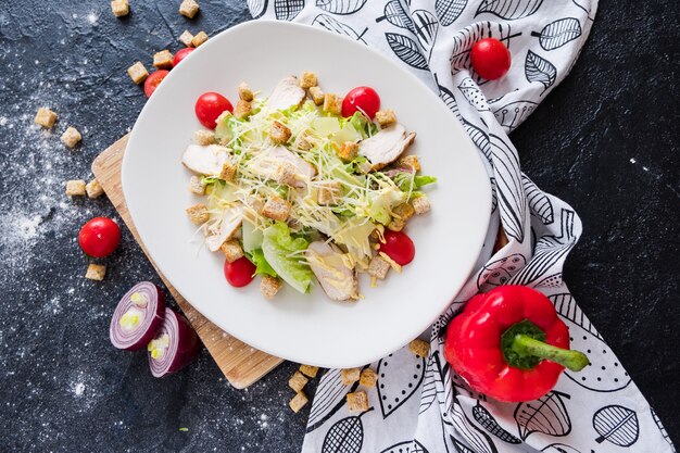 Salada de caesar fresca com galinha em uma placa branca na pedra escura.