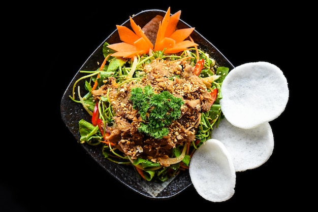 Salada de carne asiática com folhas de pennywort servida com lascas de arroz isoladas em fundo preto