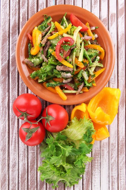 Foto salada de carne no prato com legumes em fundo de madeira