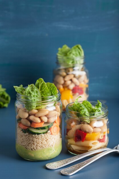 Salada de cuscuz e macarrão vegana em frascos de pedreiro com feijão de legumes