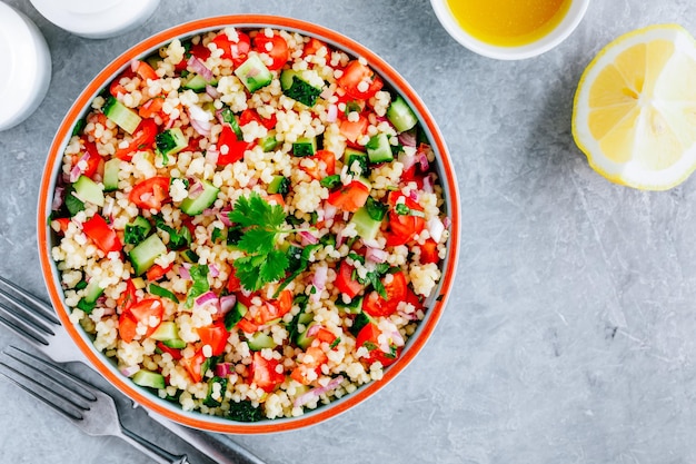 Salada de cuscuz Tabbouleh com tomates frescos, pepinos e cebolas vermelhas em tigela sobre fundo de pedra cinza