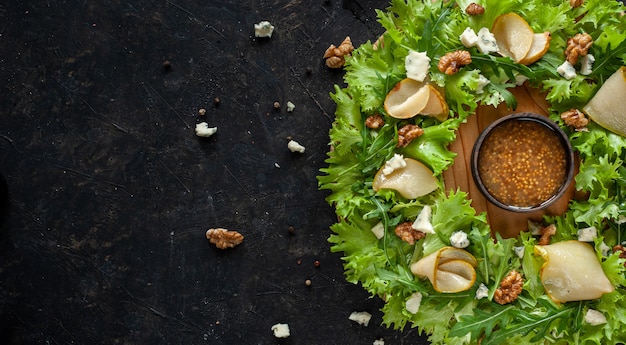 Salada de dieta leve com pêra, nozes e queijo azul. a salada é colocada na forma de uma coroa de flores sobre uma placa de madeira redonda, com o molho no centro e sobre um fundo escuro. copie o espaço. foto de alta qualidade