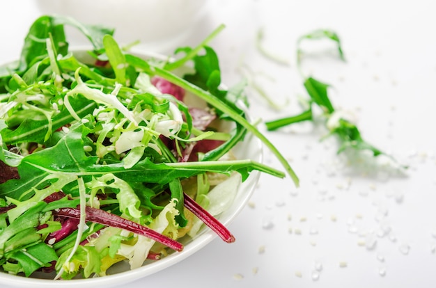 Salada de ervas frescas, rúcula, alface, sal e gergelim em tigela branca.