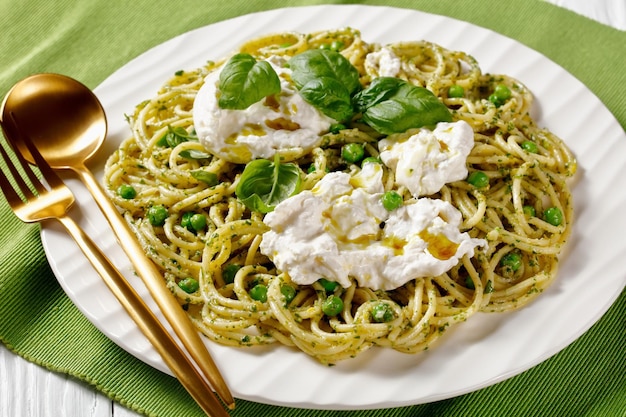 Salada de espaguete de verão com molho pesto ervilhas verdes folhas de manjericão e queijo burrata em um prato cozinha italiana closeup