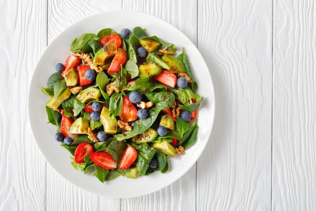 Salada de espinafre, abacate, nozes e frutas vermelhas com vinagre balsâmico e molho de sementes de papoula em um prato branco