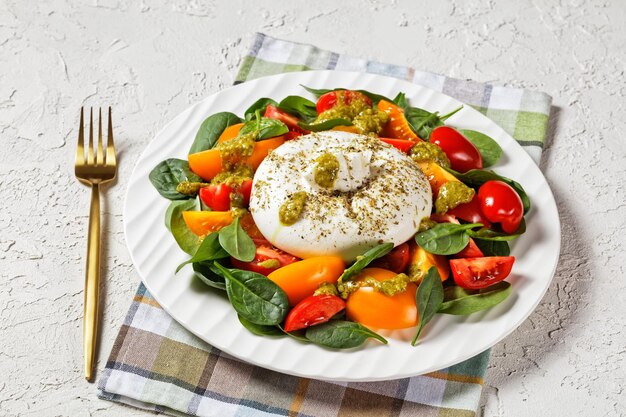 Salada de espinafre, tomate e queijo Burrata com molho pesto de manjericão em um prato, cozinha italiana