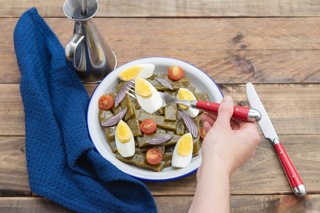 Salada de feijão verde com ovo cozido e tomate. Mão de uma mulher comendo salada. Copie o espaço. Superfície de madeira.