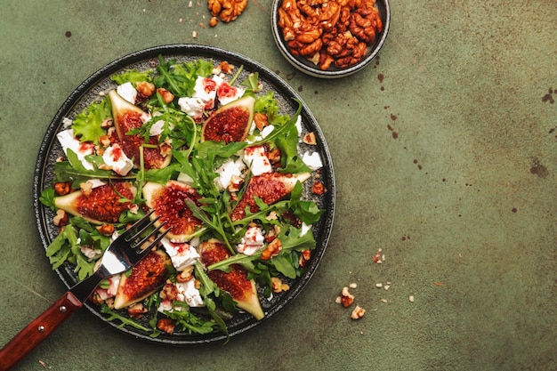 Salada de figo com queijo branco, nozes, rúcula e molho de geleia no espaço de cópia de vista superior de fundo verde ferrugem