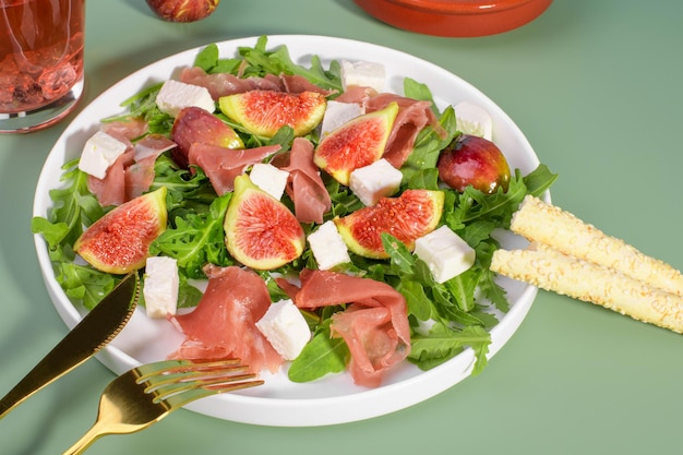 Salada de figos de outono com presunto cru de rúcula feta em prato branco sobre fundo verde servido com vinho rosé