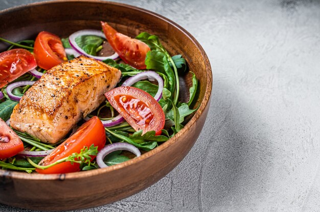 Salada de filé de salmão com folhas verdes de rúcula, abacate e tomate em prato de madeira