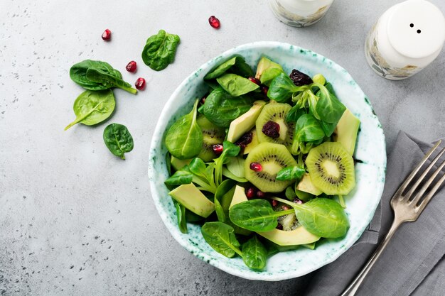 Salada de folhas de espinafre, agrião, kiwi, abacate e romã em uma velha placa de cerâmica sobre um fundo cinza de concreto