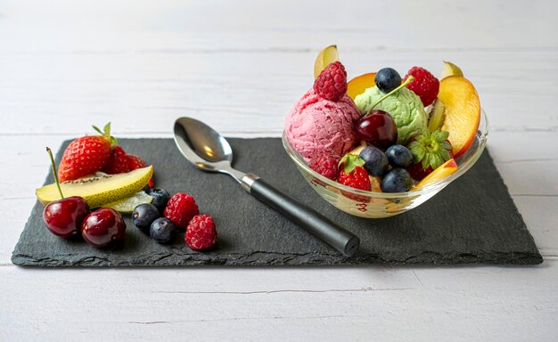 Salada de frutas com colher de sorvete de baunilha pistache de morango em uma tigela em um pedaço de ardósia é