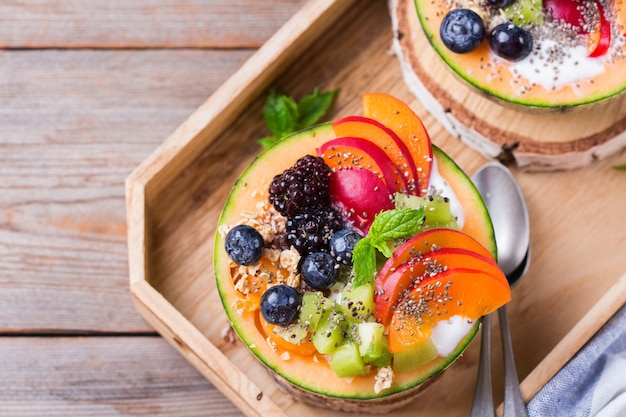 Salada de frutas com iogurte em tigela de melão esculpido na mesa