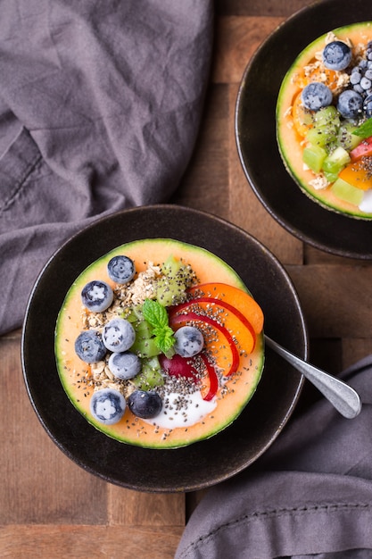 Salada de frutas com iogurte em tigela de melão esculpido na mesa