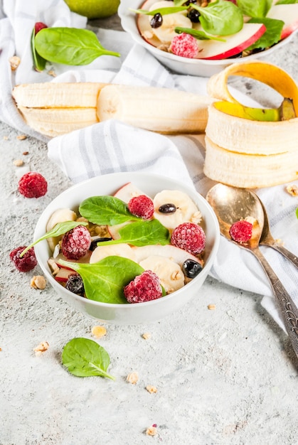 Salada de frutas e bagas saudável café da manhã de verão com espinafre granola maçã e banana fundo de mármore branco