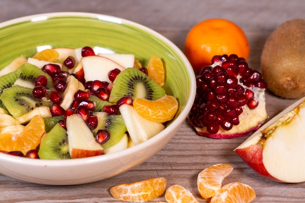 Salada de frutas em uma tigela de cerâmica e várias frutas em uma mesa de madeira Comida vegetariana superalimento cura