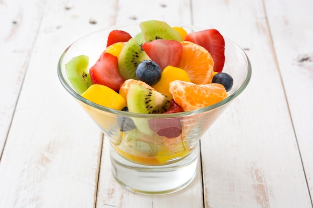 Salada de frutas em uma tigela de cristal na mesa de madeira branca