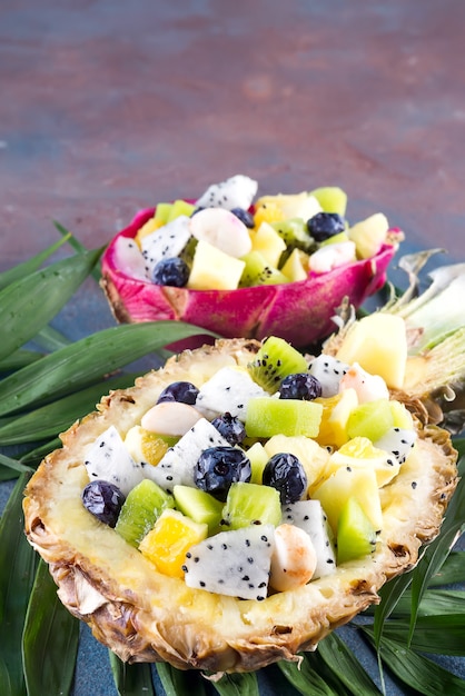 Salada de frutas exóticas servido em meio abacaxi em folhas de palmeira em fundo de pedra