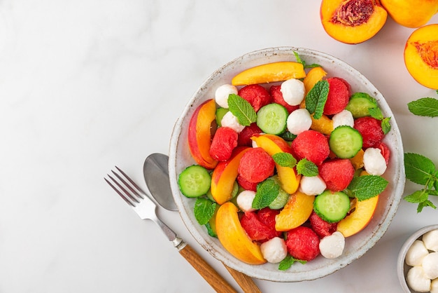 Salada de frutas frescas de verão feita de queijo mussarela de pepino pêssego melancia e hortelã em um prato