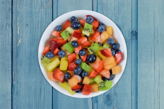 Salada de frutas frescas e alegres sobre um fundo de madeira azul