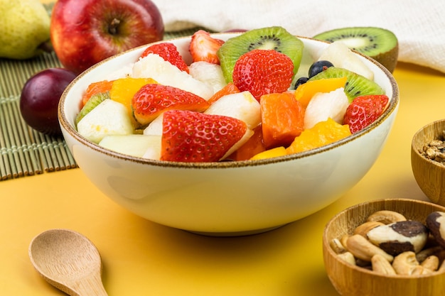 Salada de frutas frescas em uma tigela Frutas tropicais e multicoloridas Abacaxi manga uva morango mamão melão kiwi Adicional com castanhas e granola Foco seletivo
